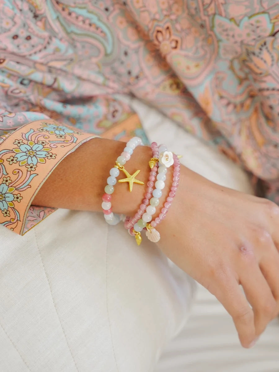 Handcrafted ocean inspired jewelry featuring pastel Kiki Bracelets with sea charms, worn on a woman's wrist.