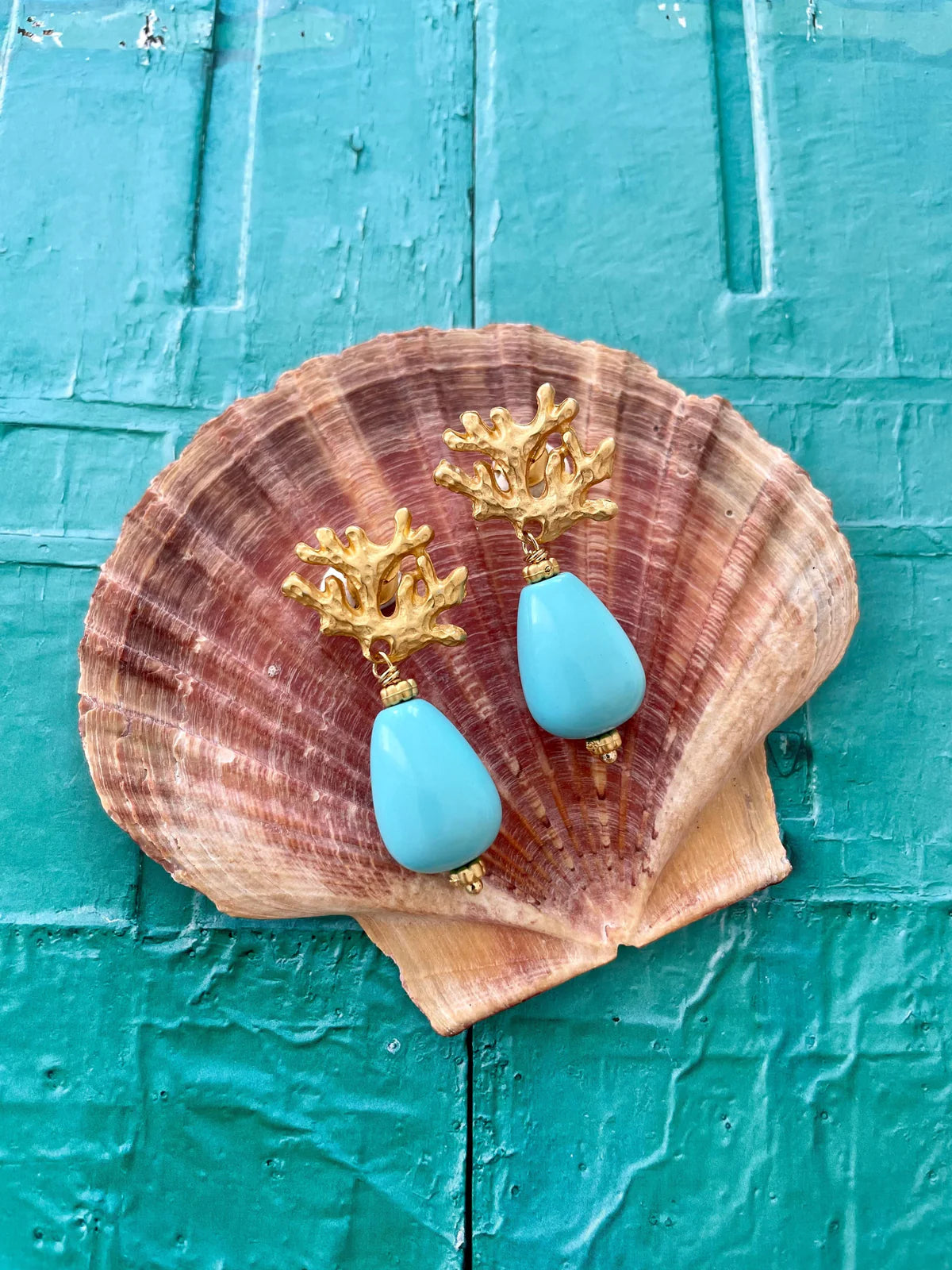 Handcrafted ocean inspired Ravello earrings with turquoise drops and matte gold coral posts on a seashell background.